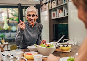 Woman with black glasses smiling while eating with friend