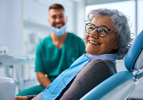 Woman with black glasses smiling while sitting in treatment chair