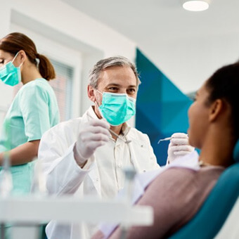 Dentist wearing mask holding dental instruments about to examine patient