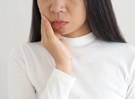 Woman in white sweater rubbing jaw in pain