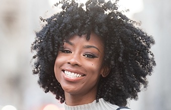 Woman with curly black hair smiling outdoors